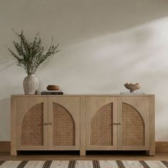 a sideboard with wicker doors and two vases on top of it next to a striped rug