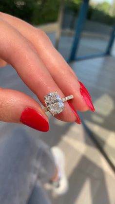 a woman's hand with red nails and a ring on her finger, holding an engagement ring