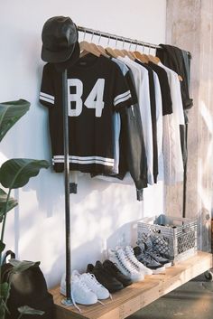 clothes and shoes are hanging on a rack in front of a wall with a hat