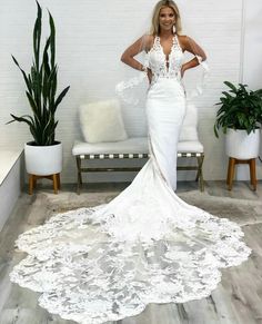 a woman standing in front of a white wall wearing a wedding dress with sheer sleeves