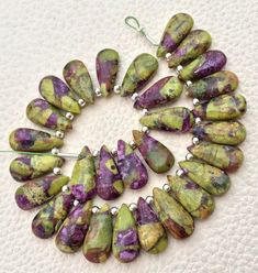 a bunch of green and purple beads are arranged in a circle on a white surface