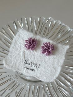 two small purple flowers are placed on top of a white napkin in a glass dish