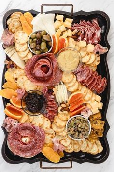 an assortment of meats, cheeses and crackers on a black platter