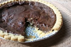 a chocolate pie with one slice missing from it on top of a cloth tablecloth