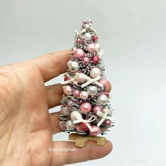 a miniature christmas tree with pink, white and silver ornaments on it's base