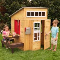 two children playing in a wooden play house with a picnic table and bbq grill