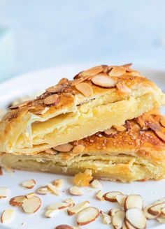 two pieces of pastry on a plate with almonds scattered around the edges and one slice cut in half