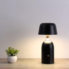 a black table lamp sitting next to a potted plant on top of a wooden table