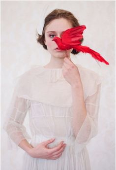 a woman holding a red bird over her face