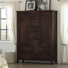 an armoire in a bedroom next to a window with curtains and pictures on it