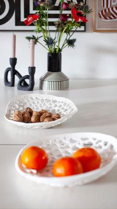 two white bowls filled with fruit and nuts on top of a table next to flowers