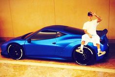 a man sitting on top of a blue sports car in front of a beige wall