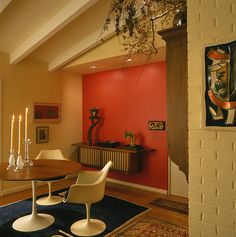 a dining room with an orange wall and white chairs in front of a wooden table