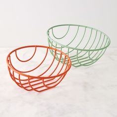 two orange and green wire baskets sitting on top of a white counter next to each other