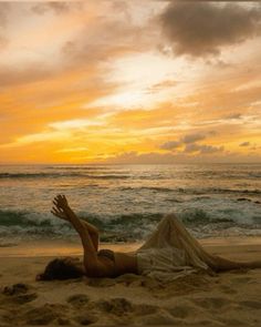 a woman laying on top of a sandy beach next to the ocean under a cloudy sky