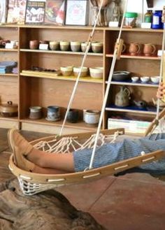 a woman sitting in a hammock on top of a wooden floor next to shelves