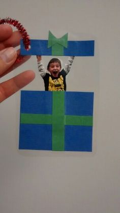 a hand holding up a piece of paper that has a photo of a boy in a gift box on it