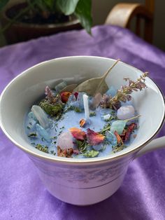 a white bowl filled with blue liquid and flowers on top of a purple table cloth