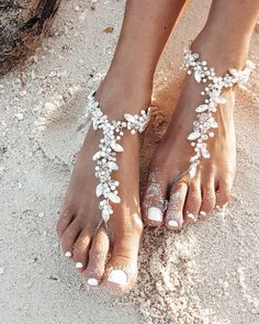 a woman's feet with white sand and flowers on their toes, in the sand