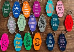 many different colored key chains are hanging on a wooden wall with words written in them