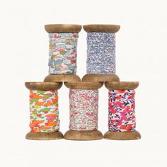 six spools of thread in different colors and sizes on a white background with wooden stand