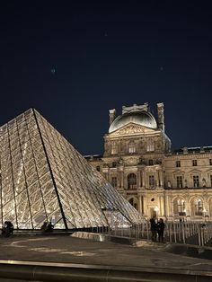 the pyramid is lit up at night in front of a large building with many windows