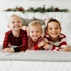 three children laying on a bed smiling at the camera with christmas decorations in the background