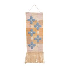 a wall hanging with blue flowers and fringes on an orange, white and yellow striped background