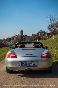 a silver sports car parked on the side of a road next to a grassy hill