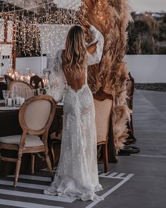 a woman standing in front of a table wearing a white dress with long sleeves and an open back