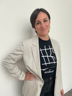 a woman standing in front of a white wall wearing a black shirt and blazer