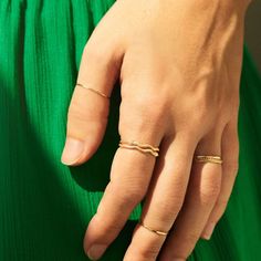 A hand rests in front of vibrant green fabric. The hand is wearing dainty gold rings stacked on eachother for a bolder look. Gold Minimalist Snake Ring For Promise, Gold Minimalist Snake Ring As Promise Ring, Modern Twist 14k Gold Stackable Rings, Minimalist Yellow Gold Snake Ring, Minimalist Yellow Gold Open Snake Ring, Gold Midi Rings With A Modern Twist, Yellow Gold Midi Rings In Recycled Gold, Elegant 14k Gold Snake-shaped Ring, Elegant 14k Gold Snake Shaped Rings