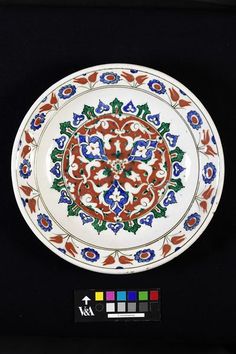 an ornate plate with red, green and blue designs on the rim is displayed in front of a black background