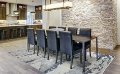 a dining room table and chairs in front of a kitchen with an exposed brick wall