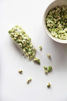 a white bowl filled with green popcorn next to a small cup full of kernels