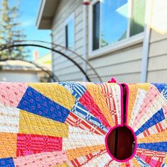 a multicolored quilt with a hole in the center on a bench outside a house