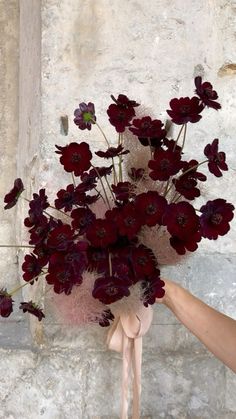 a person holding a bouquet of flowers in front of a stone wall