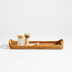 a wicker tray with two shaving brushes and soaps on the bottom, sitting on a white surface