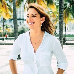 a woman standing in front of palm trees and smiling at the camera with her hands on her hips