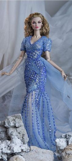 a barbie doll wearing a blue dress and veil standing on rocks with snow in the background