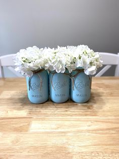 three mason jars filled with white flowers on top of a wooden table