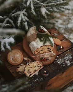 bread and other food on a wooden tray in the snow with candles around it, surrounded by pine branches