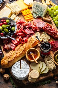 an assortment of cheeses, meats, and fruit on a wooden platter