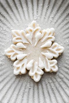 a close up of a white flower on a plate with water droplets and sand around it