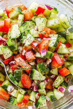 a glass bowl filled with cucumber, tomato and dill pickle salad