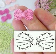 a hand holding a pair of pink crocheted bow clip on top of a piece of paper