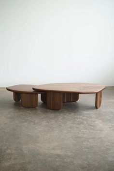 two wooden tables sitting on top of cement floor next to each other in front of a white wall