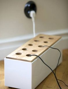 a white box sitting on top of a wooden floor next to a wall mounted power strip