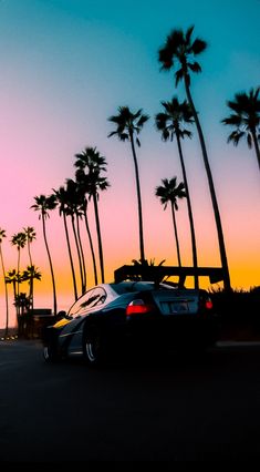 a car driving down the road with palm trees in the background at sunset or dawn