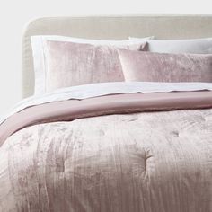 a bed covered in pink and white sheets, pillows and blankets on top of it